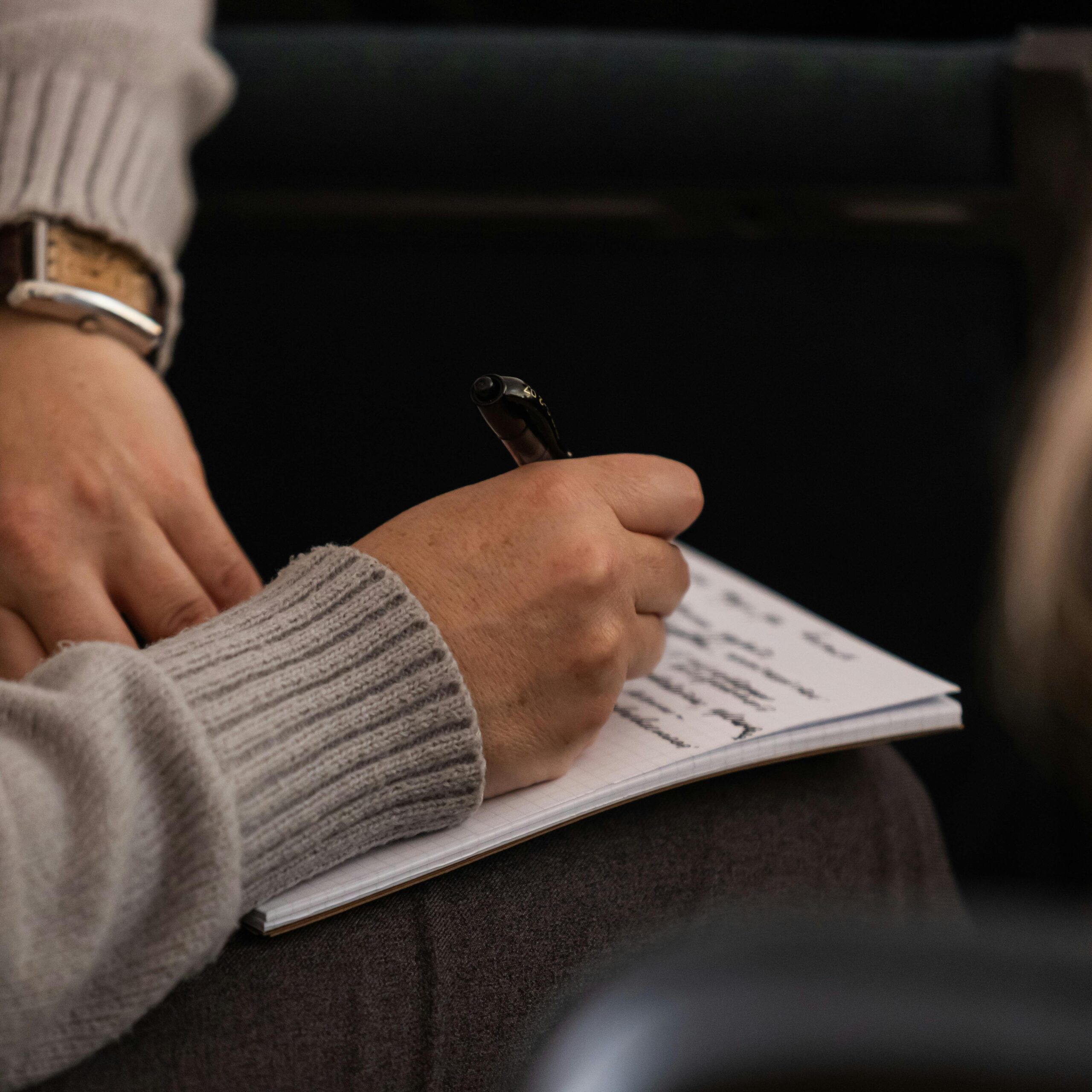 pexels-photo-31396700-31396700 Person in grey sweater taking notes in a notebook with a pen.